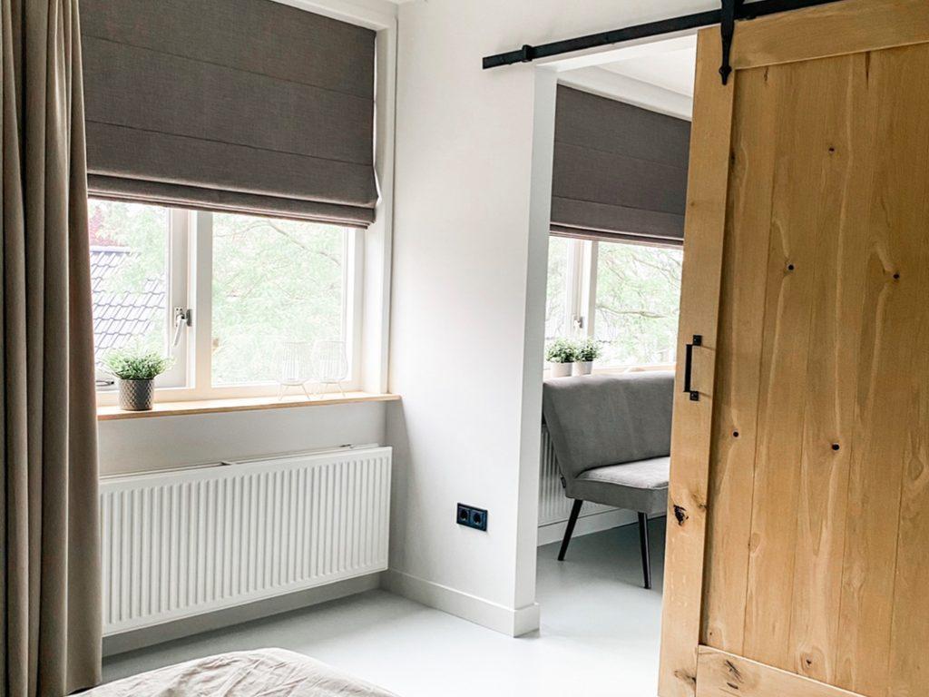 Sfeerfoto van massief eiken barndeur loftdeur aan schuifrailsysteem in een lichte en smaakvol gestylde slaapkamer. Woodstyles heeft een grote voorraad aan verschillende maten eiken barndeuren. We leveren snel in zowel belgië als nederland tegen goedkope prijzen