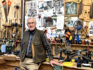 Timmerman in zijn werkplaats met een wand vol gereedschap. Meubelmaker die met eiken panelen werkt.