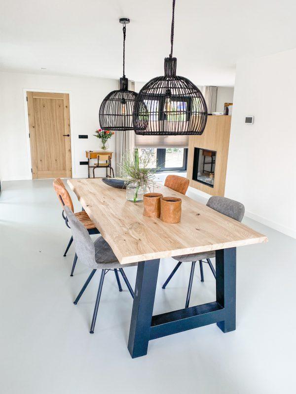 Sfeerfoto van een smaakvol ingericht interieur met als middelpunt een bij woodstyles samengestelde tafel. De tafel bestaat uit een massief eiken tafelblad van 40 mm dikte met boomstamkant en stoere zwarte stalen A-poten. Woodstyles biedt een ruime keuze aan tafelpoten en vele maten massief eiken tafelbladen. Snelle levering en scherpe prijzen